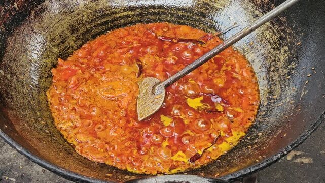 Traditional Indian Cooking in Large Iron Wok, Spicy Curry Masala Being Prepared in Outdoor Kitchen, Authentic Indian Food Preparation with Oil, Tomato and Turmeric, Street Food and Cuisine