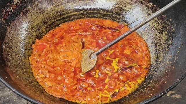 Traditional Indian Cooking in Large Iron Wok, Spicy Curry Masala Being Prepared in Outdoor Kitchen, Authentic Indian Food Preparation with Oil, Tomato and Turmeric, Street Food and Cuisine