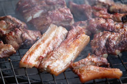 Close up of delicious pork ribs and belly grilling on a charcoal BBQ grate.A mouth-watering, close-up macro shot of seasoned pork ribs and thick pork belly slices grilling to perfection on a charcoal 
