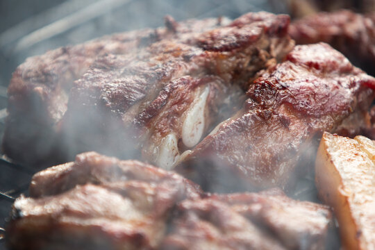 Close up of delicious pork ribs and belly grilling on a charcoal BBQ grate.A mouth-watering, close-up macro shot of seasoned pork ribs and thick pork belly slices grilling to perfection on a charcoal 