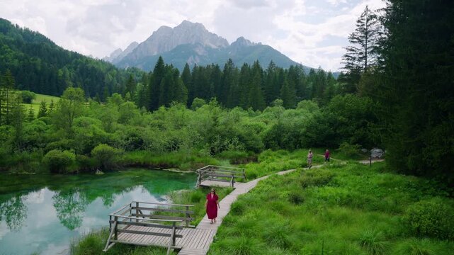 Woman Tourist Walks Along Wooden Boardwalks Beside Emerald-green Waters At Zelenci Nature Reserve In Slovenia. Aerial Wide Shot