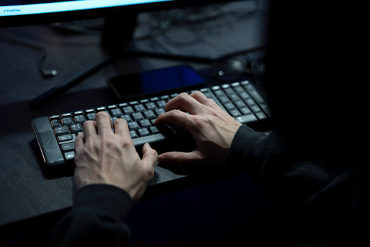 Close up of hacker's hand typing code on computer in a dark room.