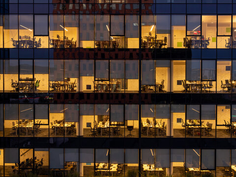 Aerial view of a modern office building facade at night with illuminated windows revealing desks and computer workstations in Gdansk, Poland.