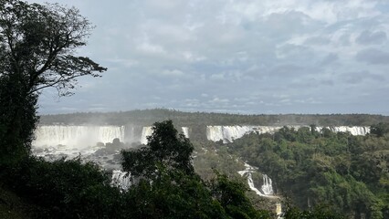 Fototapeta premium Majestic Iguazu Falls in Brazil showcasing powerful cascades amidst lush green rainforest under a cloudy sky