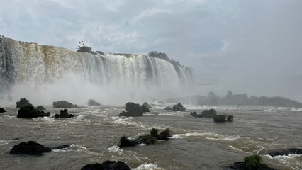 Majestic Iguazu Falls in Brazil with powerful cascades and turbulent waters surrounded by lush vegetation under a cloudy sky © Felippe Lopes