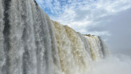 Massive Iguazu Falls cascades over cliff edge with dramatic cloudy sky and mist below © Felippe Lopes