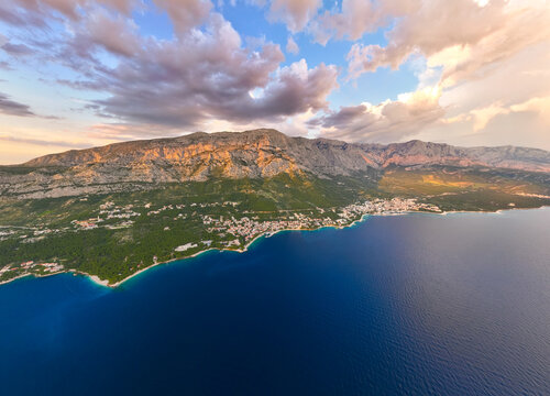 Aerial view of the coastal town of Brela nestled at the foot of the Biokovo mountains along the Adriatic Sea during golden hour in Brela, Split-Dalmatia County, Croatia.