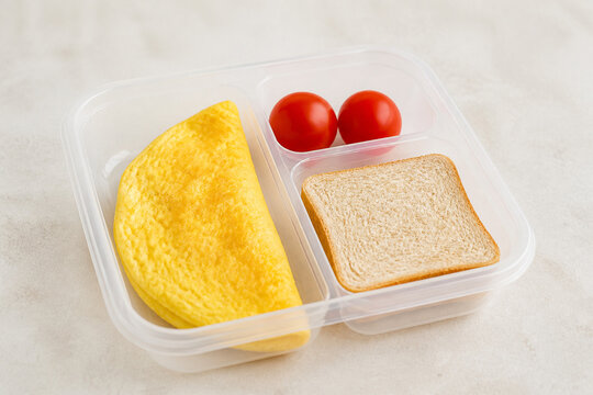 A plastic lunch box filled with a folded omelet, a piece of bread, and fresh red tomatoes. Concept for a healthy meal, school lunch, and balanced nutrition for work or daily routine.