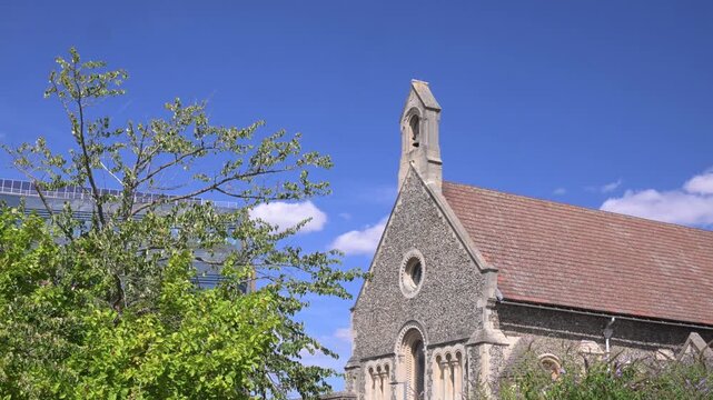 St James Roman Catholic Church roof and bell gable rise above leafy trees under a bright blue daytime sky.