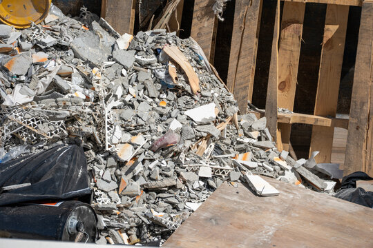 A pile of broken concrete rubble and discarded building materials mixed with wooden planks and black trash bags inside the metal container.