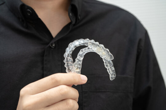 Man holding invisible aligner orthodontic retainer for dental teeth straightening.