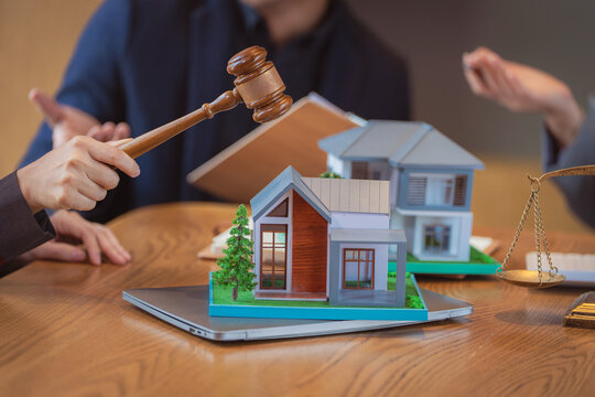 A lawyer is explaining real estate law to a client, with a house model and a judge's gavel placed nearby&mdash;a close-up shot focusing on home mortgages and property division.