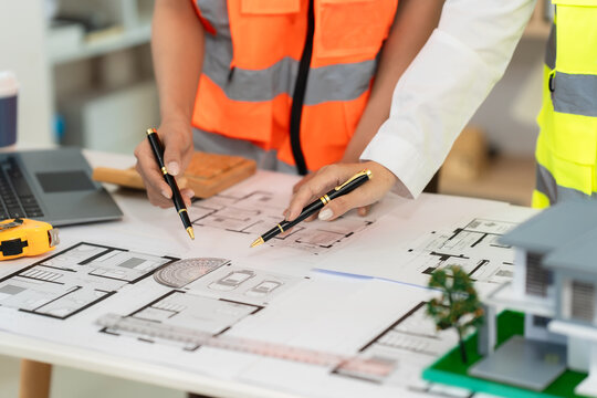 A team of architects and engineers is brainstorming an eco-friendly home design using a tablet, alongside a close-up view of a solar panel model.