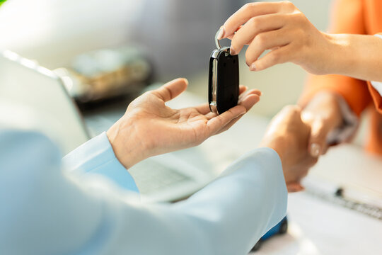 Close up of salesman giving key and shaking hands with customer after buying new car.