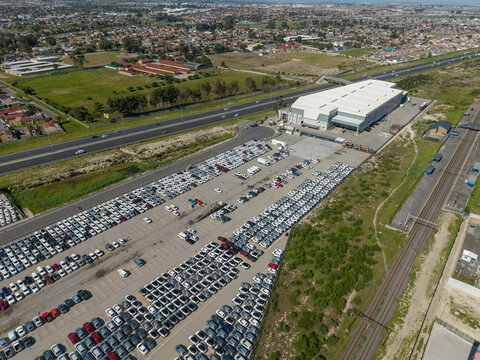 Aerial view of a large car storage lot and distribution center in Bellville South, with rows of parked vehicles, a warehouse, and highway infrastructure in Cape Town, Western Cape, South Africa.