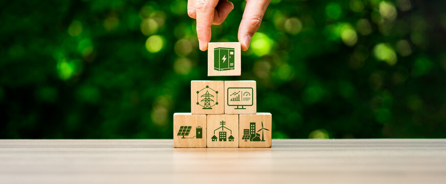 Smart grid and battery storage concept with hand placing power cabinet icon cube on wooden pyramid blocks showing renewable energy infrastructure and sustainable electricity management
