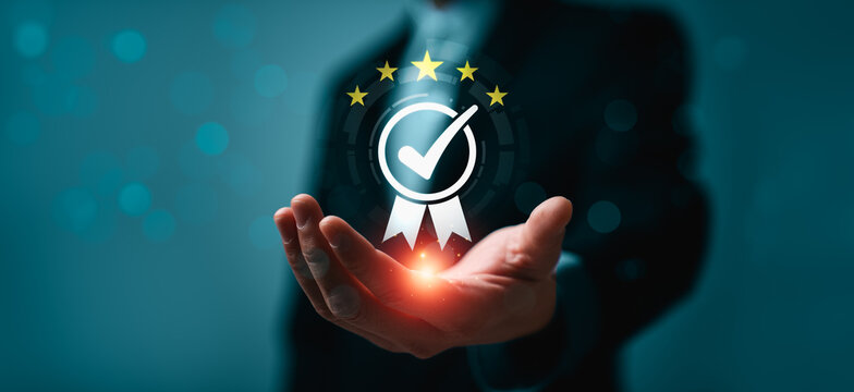 Business hand presenting virtual quality assurance badge with checkmark and five stars in futuristic interface, representing certification standard compliance, trust, approval and service excellence