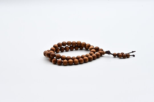 A wooden prayer bead rosary with brown beads and a tassel, arranged in a loop on a white background.