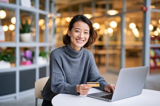 Smiling young woman using laptop and credit card at cafe table.