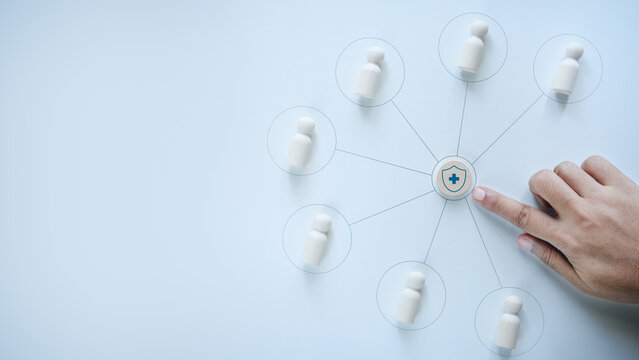 Hand touching central health insurance shield icon connected with wooden peg dolls representing employee team, concept of corporate health insurance, employee benefits, and group medical protection.