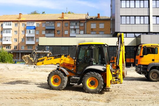 Yellow excavator at a construction site near residential buildings and a parked truck, highlighting urban development and construction activity on a clear day