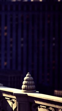 A building features a decorative element on its rooftop. In the background, tall buildings rise against the skyline. Light reflects off surfaces during daytime hours.