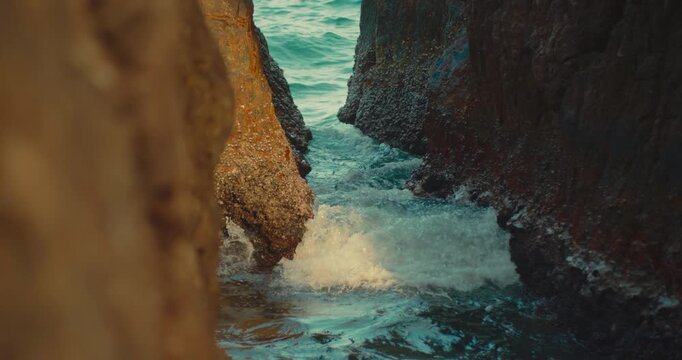 Narrow rocky sea gorge with ocean waves flowing through steep dark stone cliffs. Dramatic and moody coastal geology and rugged environmen