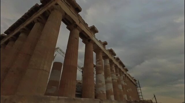 Static dramatic low angle wide shot of the iconic Doric marble columns of the Parthenon temple at the Acropolis in Athens, Greece, reaching toward a moody overcast sky with stormy clouds.