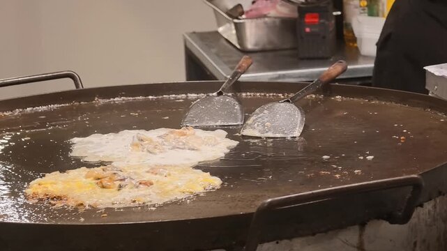 Cooking Thai crispy fried mussel omelette on a large flat griddle