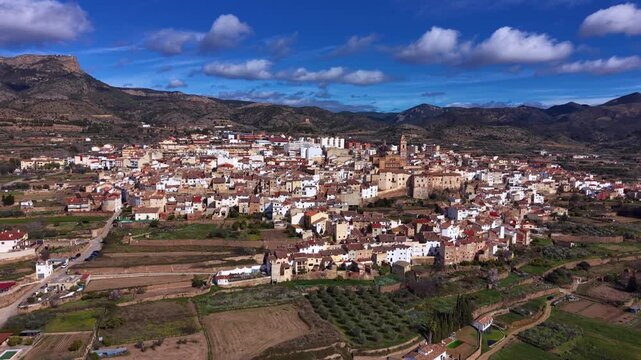Chelva, a traditional Spanish village in the Valencia region, nestled among mountains with terracotta rooftops, church tower, farmland and blue skies with white clouds