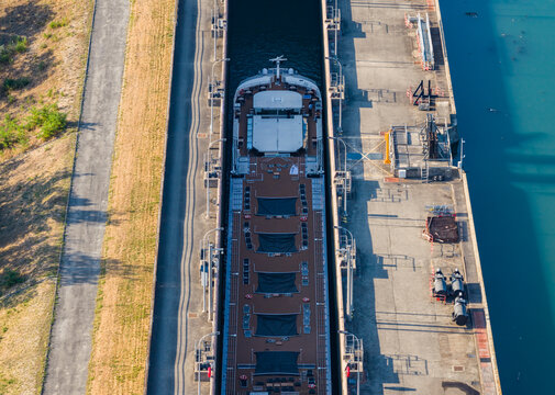 Aerial view of a river cruise ship inside a navigation lock, showing the vessel deck and surrounding waterway infrastructure in Saulce-sur-Rhone, Auvergne-Rhone-Alpes, France.