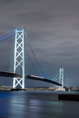 Naklejka premium 兵庫県淡路島から望む夜の明石海峡大橋。ライトアップされた世界有数の吊り橋が海面を照らす幻想的な風景。 