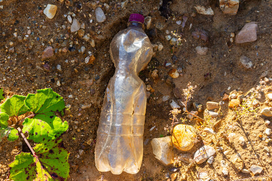 Discarded crumpled plastic bottle lying on sandy rocky ground representing environmental pollution, nature contamination and ecological disaster with trash abandoned in wild landscape