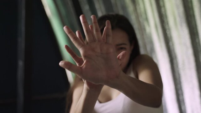 Unhappy and frightened Asian young woman hands raised in fear to stop violence and prevention from rights violations with worried sadness and depression stress in her room at home. Violent concept. 