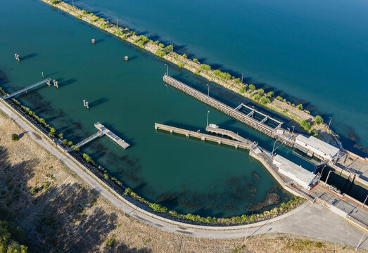 Aerial view of navigation barriers and guiding structures at the entrance to a river lock on the Rhone river, featuring concrete piers and calm water in Saulce-sur-Rhone, Auvergne-Rhone-Alpes, France.