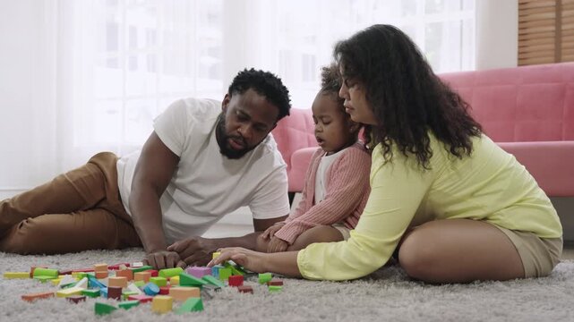 Family day concept. Happy African American father, mother, and child daughter sitting and playing with multicolored wooden blocks together with love and bonding on the floor in the living room at home