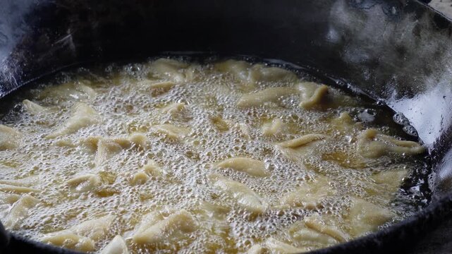 Samosas sizzling in hot oil inside giant wok