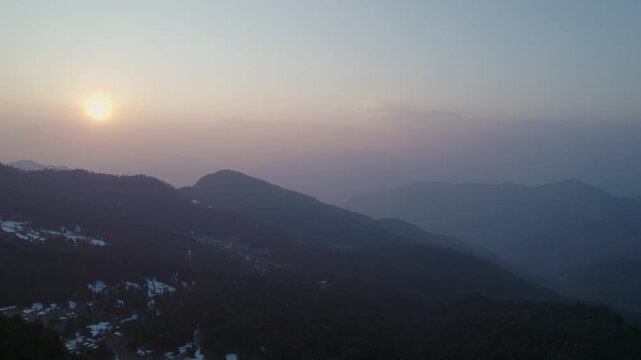 Aerial view of the snow-capped Himalayan mountain range at sunset with golden light over the peaks and hazy valleys in Rudraprayag, Uttarakhand, India.