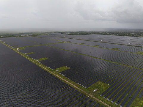 Aerial view of a large solar farm with rows of photovoltaic panels stretching across a green landscape under a cloudy sky in Miami, Florida, United States.