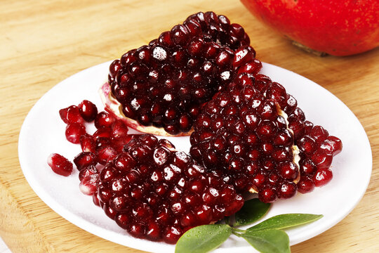 Fresh Yunnan Pomegranate Seeds and Arils on White Plate with Natural Wooden Background