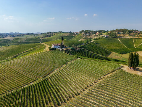 Aerial view of Tenuta La Court in the Langhe wine-growing landscapes, featuring rolling hills covered in lush green vineyards under a clear blue sky in Castelnuovo Calcea, Piedmont, Italy.