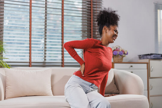 Woman experiencing lower back pain sitting on sofa