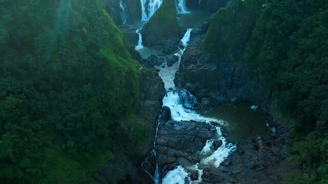 Aerial view of Barron Falls cascading through a lush tropical gorge with rocky cliffs and dense rainforest vegetation in Kuranda, Queensland, Australia.