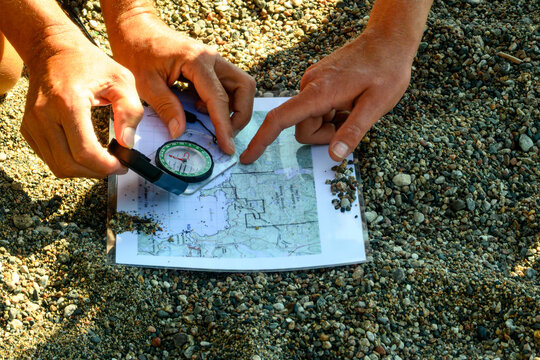Close-up of hands using a compass and topographic map to take a bearing on a remote wilderness beach