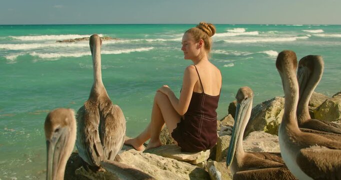 Young woman relaxes with brown pelicans on the rocky beach in Yucatan peninsula Mexico