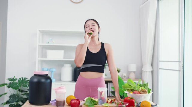 Energetic young female live streaming plant-based diet tutorial using smartphone. Asian wellness vlogger showing fresh vegetables for healthy sports nutrition and vitality.