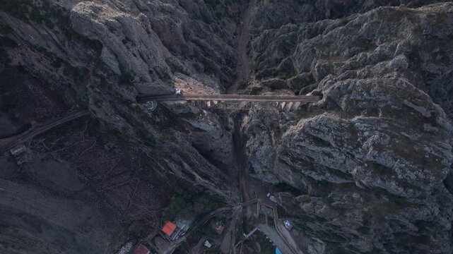 Narrow bridge spans rocky canyon with steep walls and distant path under cloudy sky for infrastructure adventure landscape nature drone photography footage premium stock content file