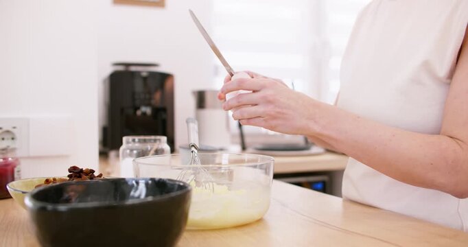 Cooking breakfast. Preparing dough. Female chef hand cracking eggs in glass bowl mixture with metal knife on modern kitchen table.