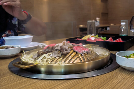 Sliced pork grilling on brass BBQ pan in restaurant. Thinly sliced pork and lard being grilled on dome shaped brass pan with boiling broth in the side moat with shredded cabbage. Asian dining culture,