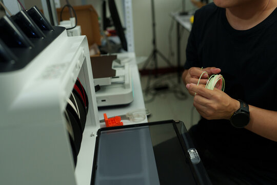 The focus is on the hands of a technician setting up a 3D printer to print a clear white plastic model, using cutting-edge technology and concentrating on specific points within the laboratory.